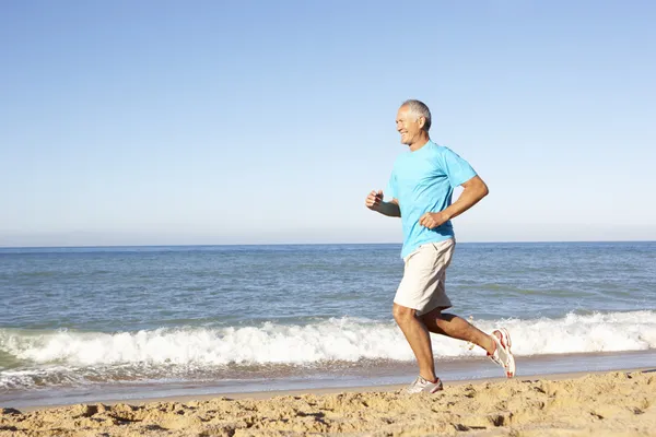 Starszy człowiek w odzież fitness, biegnącej wzdłuż plaży — Zdjęcie stockowe
