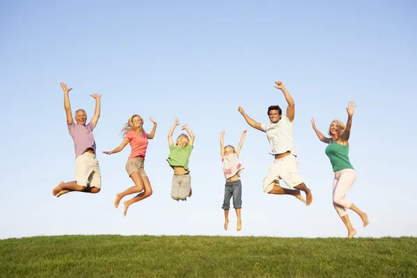 Young couple with grandparents and children jump in a field — Stock Photo, Image