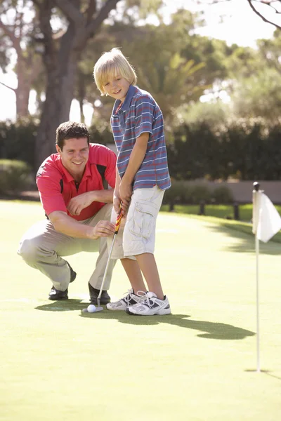 Padre enseñando hijo a jugar golf en poner en verde Imagen de archivo