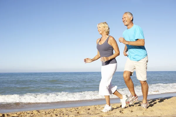 Senior koppel in fitness kleding loopt langs de strand Stockafbeelding