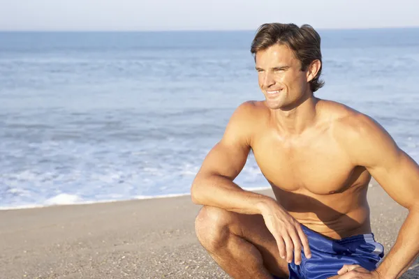 Человек сидит на пляже расслабляясь — стоковое фото