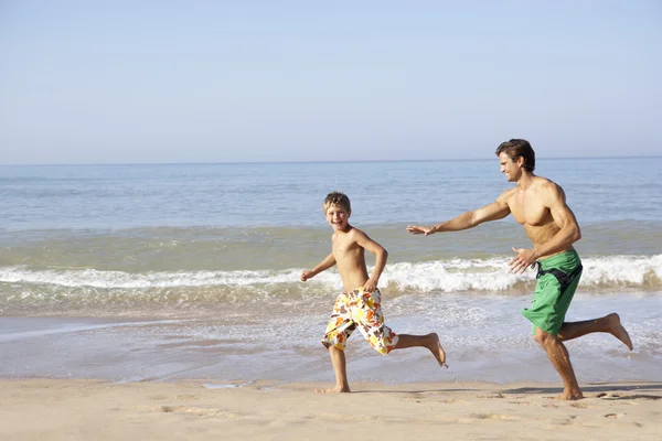 Father chasing young boy on beach — Stok fotoğraf