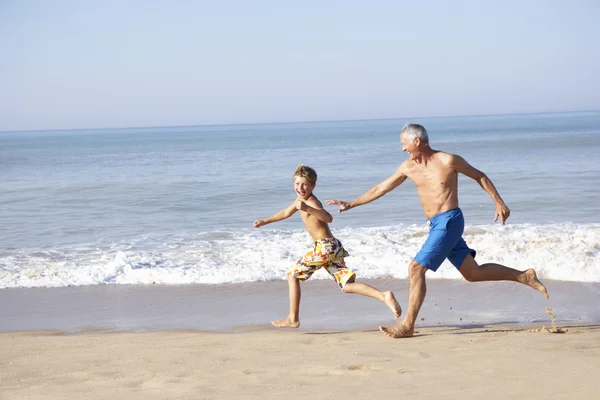 Grandfather chasing young boy on beach — Stok fotoğraf