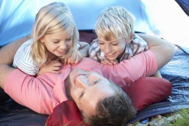 Young father plays with children in tent clipart