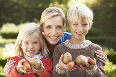 Young mother and children in garden pose with vegetables clipart