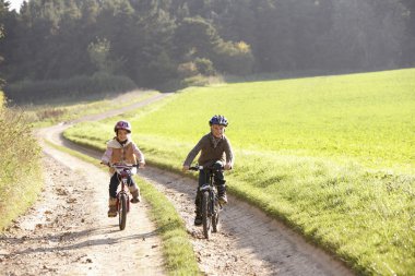 Two young children ride bicycles in park clipart