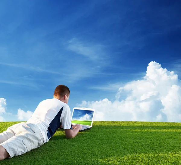 Genç adam yeşil alan üzerinde bir dizüstü bilgisayar kullanmak — Stok fotoğraf
