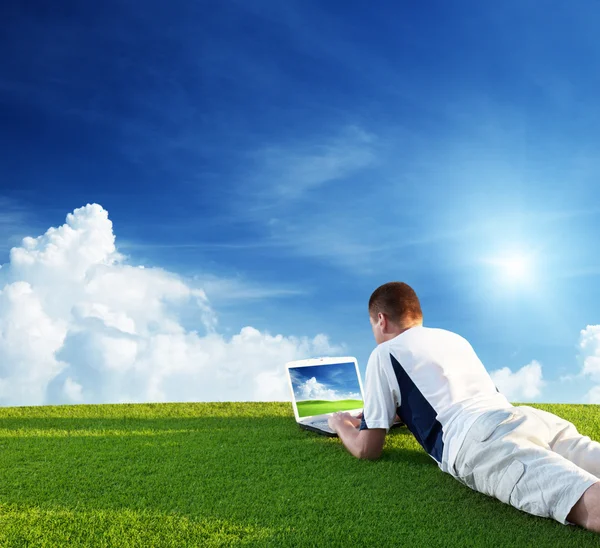 Молодой человек использует ноутбук на зеленом поле — стоковое фото