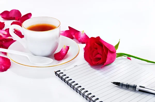 Cup of coffee with red roses and notebook on white background