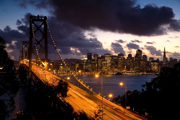 時間経過イメージ ベイブリッジ日没時 サンフランシスコでトレジャー アイランドからバック グラウンドでの — ストック写真