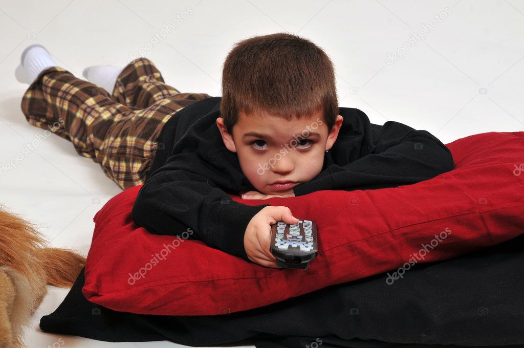 Young boy lounging with pillows on the floor, watching television with remote control in hand.
