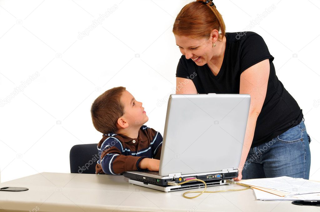 Mom smiling at son sitting at a desk with boy at laptop doing good work.