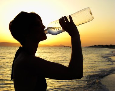 Silhouette of a Woman drinking Water on the Beach clipart