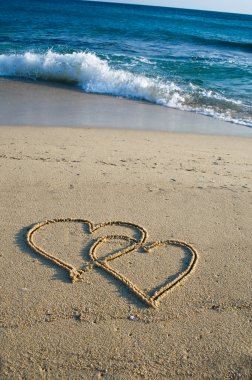 Two ensambled hearts drawn in the sand of a beach clipart