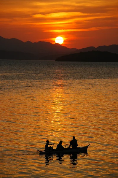 stock image Silhouette of three men in a dinghy at sunset