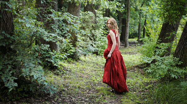 Woman in a red evening gown walks in the woods