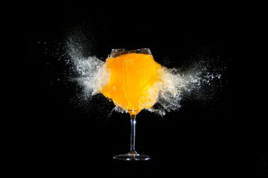 Glass with orange juice explosions at the black background clipart