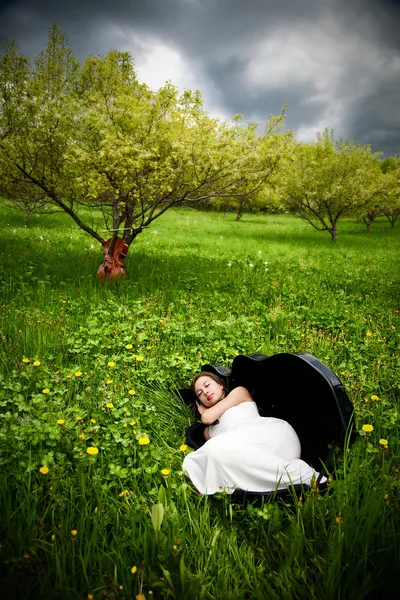 チェロのバック グラウンドでリンゴ園でチェロのケースで眠っている美しい女の子 — ストック写真
