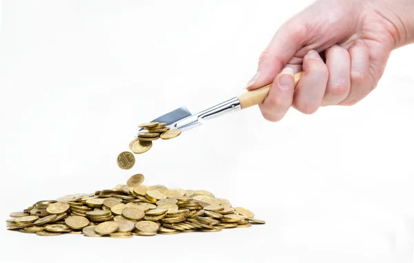 Mão com pá espalhando moedas na pilha — Fotografia de Stock