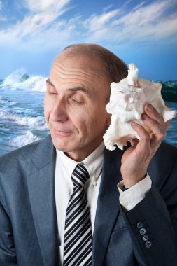 Businessman listening to the shell and ocean behind him clipart