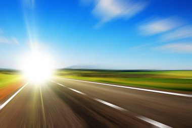 Blurred road and blue blurred sky with a shining sun clipart