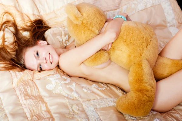 Vrouw met een teddybeer op bed Stockafbeelding