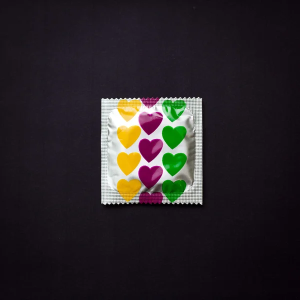Kondom mit Herzen auf schwarzem Hintergrund — Stockfoto