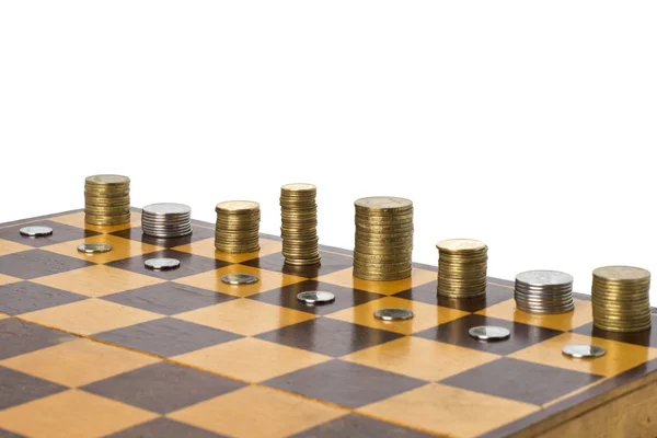 stock image Piles of coins on old chessboard on white