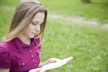 Genç bir kadın parkta kitap okuyor.