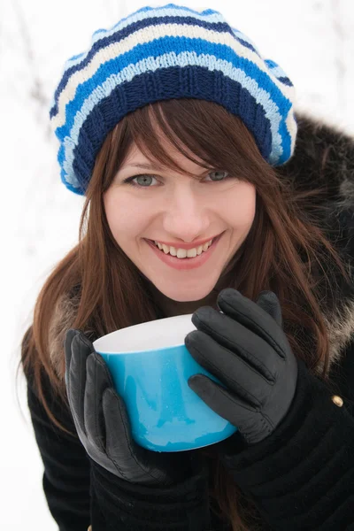 縞模様の帽子と手袋 笑みを浮かべて ブルーのカップを保持している若い女性 — ストック写真