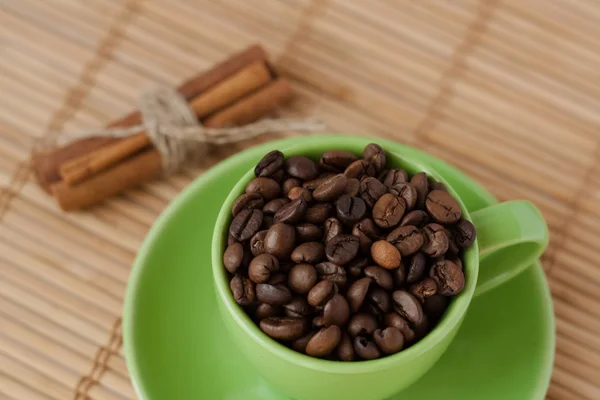 Coffee beans and cinnamon stick in a green cup — Stock Photo, Image