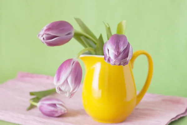 Delicate bouquet of purple tulips in a yellow jug — Stock Photo, Image