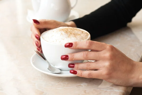 Coupe du matin de cappuccino et la main d'une fille avec des ongles rouges et une bouilloire Images De Stock Libres De Droits
