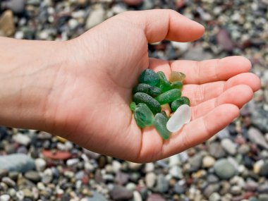 A small hand collects green stones on the beach clipart