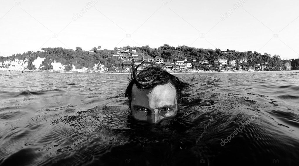 Half black and white face of a man out of the water with beach in the background