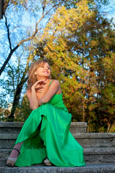 緑の服で美容女性秋の公園での階段の上に座る — ストック写真