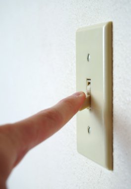 A single light switch on a white wall at an angle with a finger flipping it down, to turn it off and save power. clipart