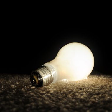 Unscrewed illuminated light bulb on the floor, brightly lit in the darkness. Black background copyspace above. clipart
