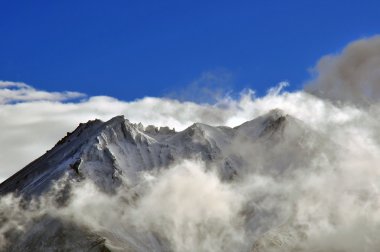 Snowy mountains with cloud coverage and blue sky in background. clipart