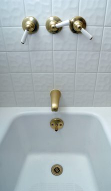 New golden bathtub valves on white tile clipart