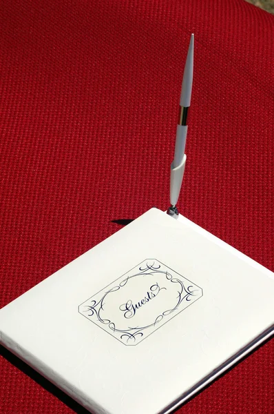正面に ゲスト と書かれた白い本を閉じ ペンが立っています 赤いテーブルクロスの上にある — ストック写真
