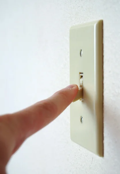 オフにし電力を節約する それをひっくり返すこと指の角度で白い壁に単一の電灯のスイッチ — ストック写真