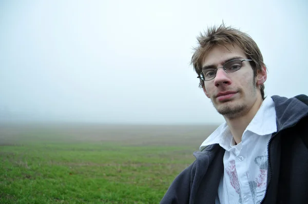 一个年轻成人站立在一个绿色的雾领域 带着微笑看着相机 这使得良好的背景 — 图库照片