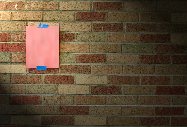 一张空白的热粉红色的纸粘在一堵砖墙与蓝色胶带 — 图库照片