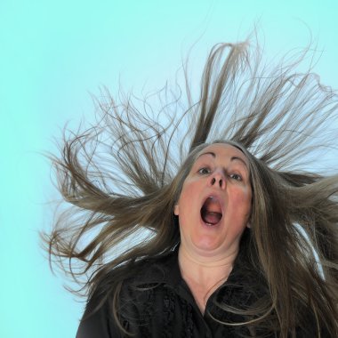 A woman screaming in front of a blue background with her hair blasting behind her. clipart