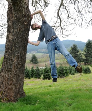 Young man holds himself on a tree while levitating above the ground clipart