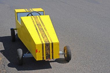 A yellow soapbox derby race cart on a racing track. clipart