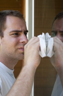 A young man cleaning the window on his house with a paper towel. clipart