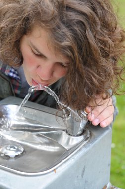 Teenager drinks from a drinking fountain clipart