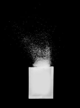 A ripped open sugar packet with sugar crystals spilling out, isolated on black background clipart